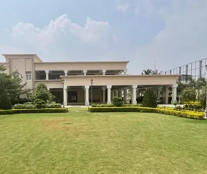 The full expanse of a luxury residence in Tirupur, featuring a large manicured lawn that provides a green foreground to the classical-inspired architecture.