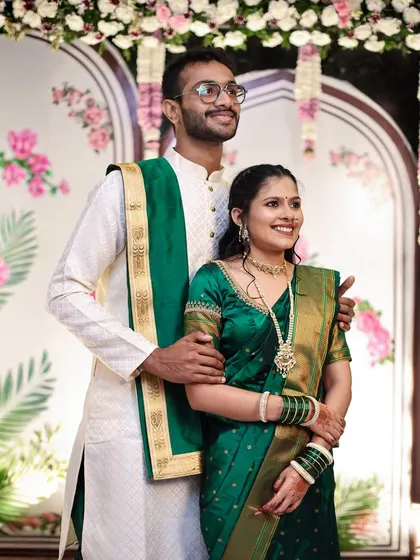 A traditional portrait of an engaged couple in matching green and white outfits, posing gracefully.