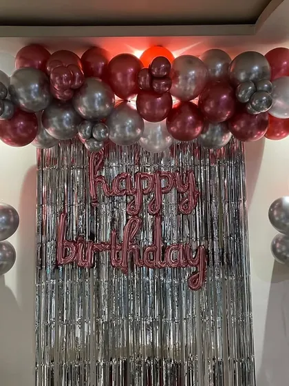 A simple birthday backdrop with a balloon garland in metallic pink and silver over a foil curtain.