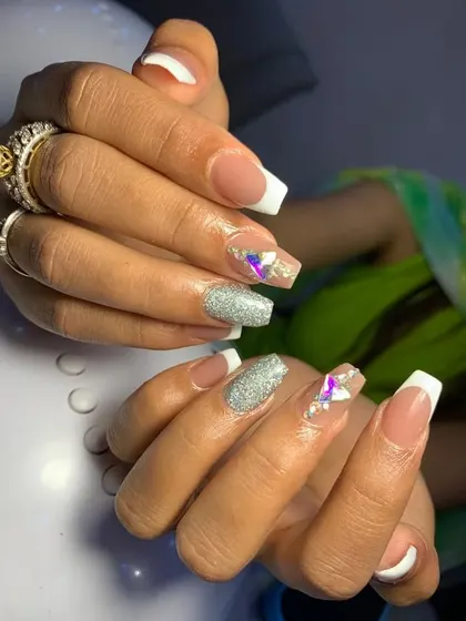 Learn classic French manicures with a modern twist. This example combines the traditional white tip with accent nails featuring silver glitter and iridescent crystal embellishments, a popular choice for bridal parties.