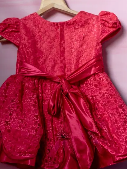 A vibrant fuchsia dress with a textured lace overlay. The dress is cinched at the back with a wide satin sash, creating a beautiful and festive party look.