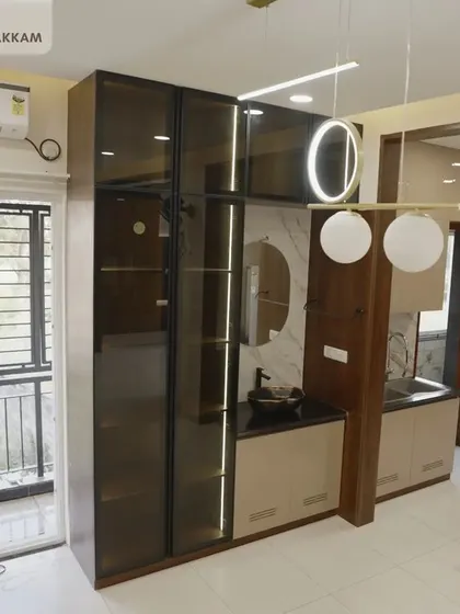A sophisticated crockery unit in the Ayyapakkam villa, featuring tall, tinted glass cabinets, a built-in wash basin, and modern pendant lighting.