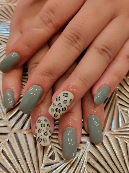 A stylish and modern set of square nails. The muted green polish is paired with accent nails featuring a classic black and white leopard print.