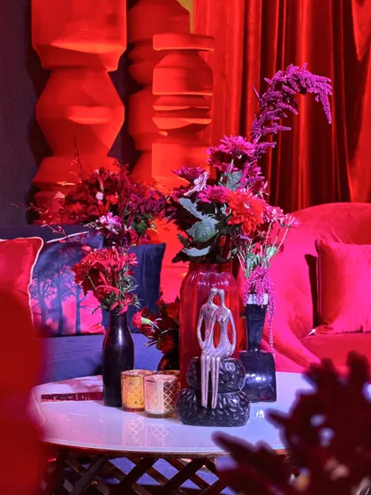 A close-up of a lounge table with unique decor pieces, including a couple's sculpture and geometric vases, all bathed in the Sangeet's signature red glow.