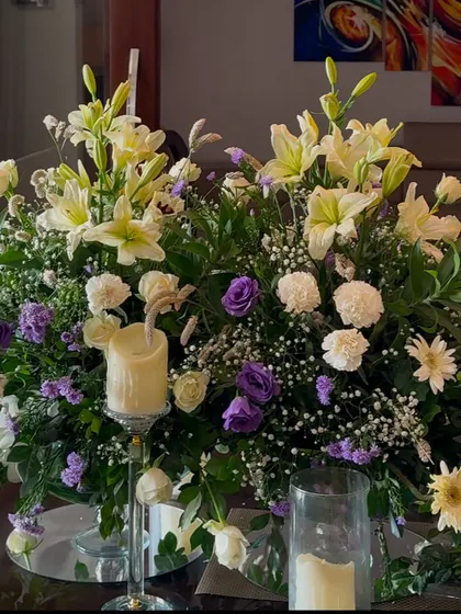 A centerpiece combining white lilies, purple roses, and baby's breath, with a thick pillar candle for a classic and romantic look.