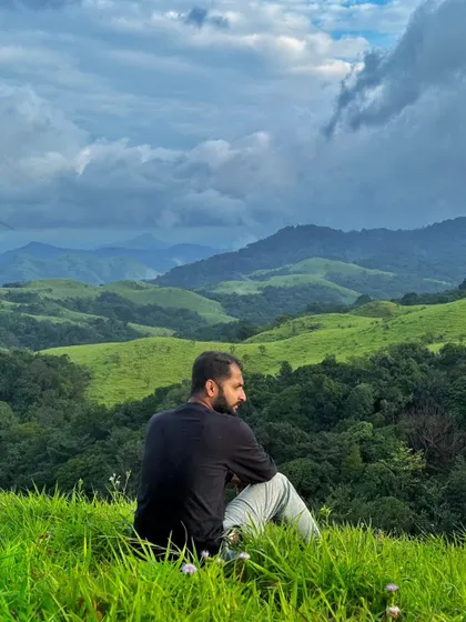 A photo of me looking out over the rolling green hills of the Western Ghats under a dramatic cloudy sky. This is a moment of peace and reflection during my travels.