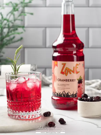 This cranberry drink is shot against a clean, white-tiled background for a fresh and modern look. The bright red of the drink pops, making it look vibrant and flavorful.