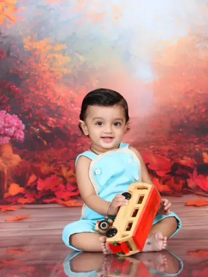 A baby boy in a light blue outfit plays with a wooden bus in the autumn forest. The contrast between his outfit and the warm background makes the photo pop.