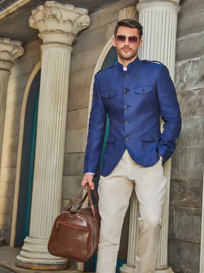 Ready for travel, this look combines the deep blue Jodhpuri jacket with a leather duffel bag, embodying a lifestyle of adventure and style.