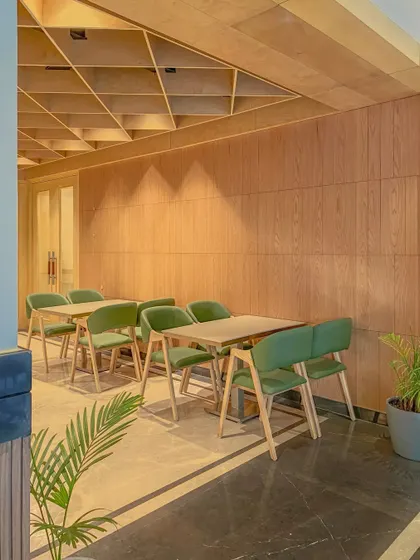 A quiet dining nook in the Bhopal hotel lobby area. The geometric wood ceiling and warm wall paneling create a cozy and architecturally interesting space for a small meal or coffee.