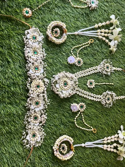 A full view of the white and green floral jewellery set. This design includes a kamarband (waist belt), necklace, hath phool, and maang tikka.