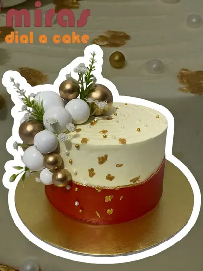 A sophisticated two-toned cake in red and white. The design is elegantly decorated with a cluster of white and gold spheres and a touch of gold leaf for a modern, festive look.