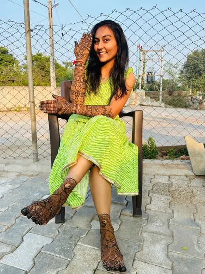 A happy bride enjoying the sun with her full bridal mehendi. The dark, rich stain of the natural henna is clearly visible on both her hands and feet.