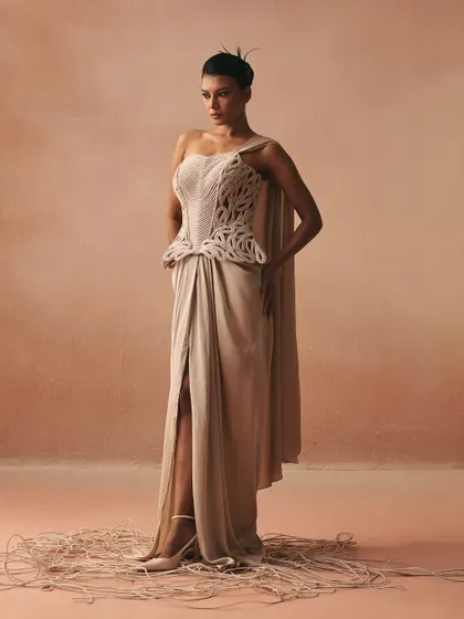 This draped gown features a one-shoulder silhouette and a thigh-high slit, with a structured, cord-embroidered corset that adds a sculptural element to the fluid design.