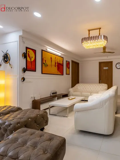 This living room exudes classic elegance with white Chesterfield sofas and tufted leather ottomans. The space is personalized with vibrant wall art and a beautiful crystal chandelier.