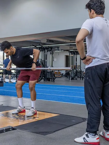 A trainee performs a bent-over row under the watchful eye of a UKSCA assessor, focusing on proper form for strength development.