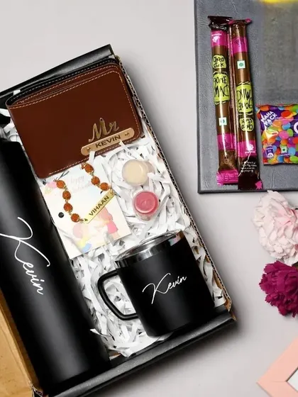 A premium Rakhi combo featuring all-black personalized items. This set includes a custom name bottle, a metal mug, a wallet, and a Rudraksha rakhi, complete with chocolates and a Rakshabandhan card.