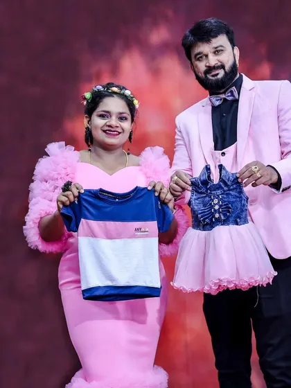 A fun gender reveal photo. The expecting couple holds up tiny blue and pink outfits, dressed in matching pink attire.