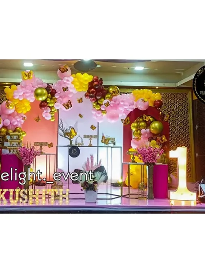 A beautiful butterfly garden theme for a first birthday celebration. This decor uses a soft pink and yellow balloon arch accented with delicate butterfly cutouts, a light-up number '1', and modern stands for a sweet and elegant party.
