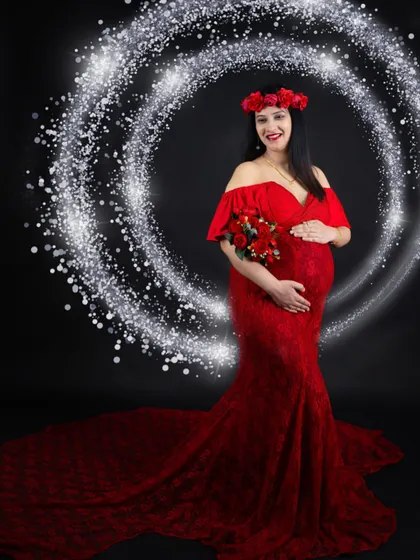 A stunning portrait in a red lace mermaid gown. The sparkling light effect adds a touch of magic, perfectly framing the mom-to-be and her floral accessories.