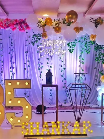 Celebrating a remarkable 85th birthday. This elegant setup features a floral and balloon arch, a "Happy Birthday" neon sign, and large marquee numbers.