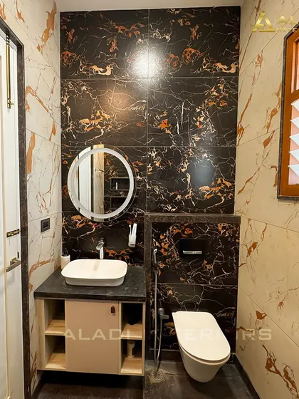 A luxurious bathroom featuring walls tiled with dramatic black and gold marble. A simple round mirror and white vessel sink provide a beautiful contrast.