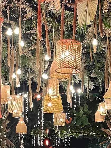 A close-up of the ceiling decor for a boho-themed reception. A mix of macrame hangings, bamboo lanterns, and Edison bulbs creates a warm, eclectic, and stylish ambiance.