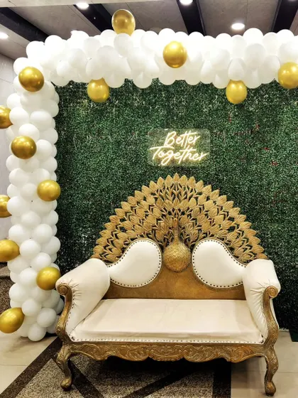 A classic and elegant "Better Together" setup for an anniversary. The greenery wall, white and gold balloons, and ornate peacock-style bench create a timeless look.