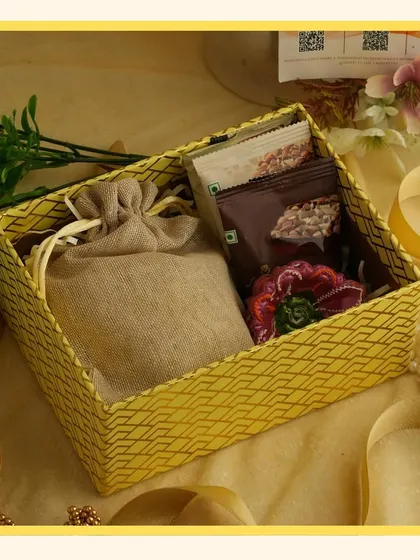The contents of the yellow gift box, including a jute potli bag and small snacks, offering a rustic and cheerful vibe.