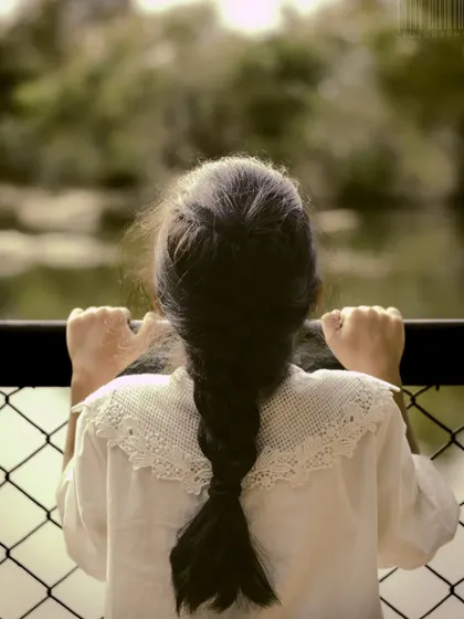 A simple, quiet moment of a young girl looking out over the water. This faceless portrait focuses on her braid and posture, evoking a sense of curiosity and wonder.