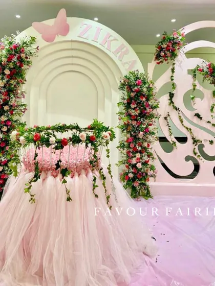 A magical butterfly-themed Aqeeqah for baby Zikra. The centerpiece is a cradle decorated with a pink tulle skirt and fresh flowers, set against elegant white arched backdrops.