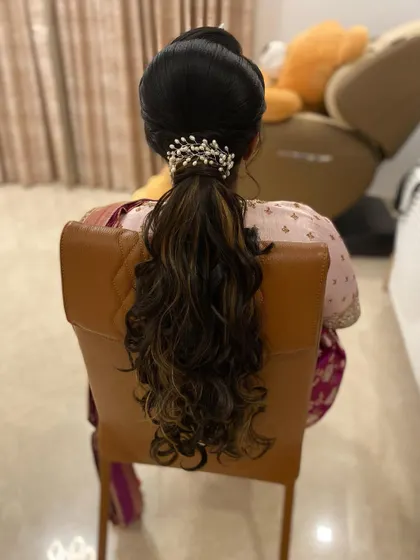A sleek ponytail with a bouffant top and curled ends, accessorized with a pearl clip. This is a sophisticated and polished look, perfect for a formal event.