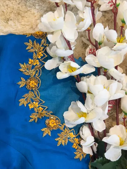 Detailed floral embroidery in gold thread and sequins on the neckline of a bright blue blouse.