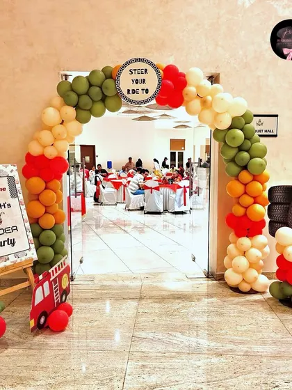 The entrance to the 'Cars' party, featuring a balloon arch in theme colors, a personalized welcome sign, and fun props like a stack of tires.