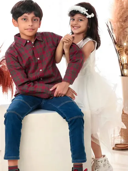 A sweet pose from a brother and sister. He sits protectively while she playfully peeks from behind him, showing their lovely bond.