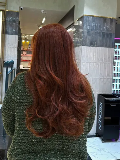 The final result of the amber hair transformation. The color is warm, rich, and has beautiful dimension, styled with soft waves.