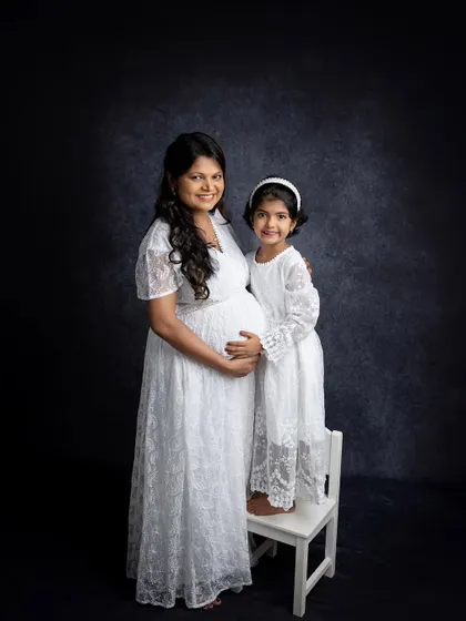A beautiful mother-daughter portrait during a maternity session. They are wearing matching white lace dresses, creating a sweet and coordinated look that celebrates their bond.