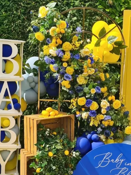A beautiful floral installation for the baby shower, combining yellow and blue flowers with fresh lemons in wooden crates for a rustic, Mediterranean feel.