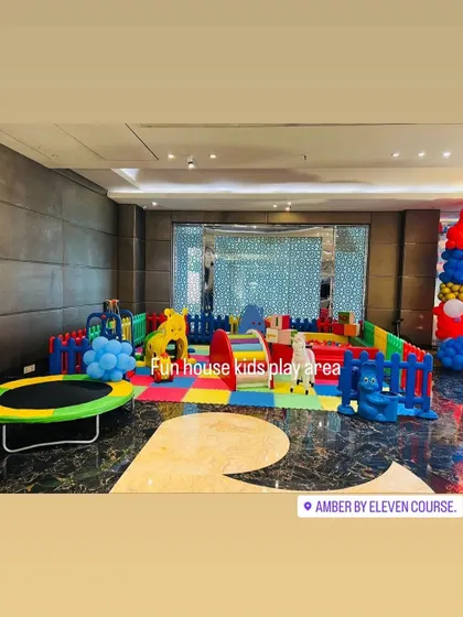 A large rainbow play area set up in a modern indoor venue, complete with a trampoline and multiple ride-on toys.