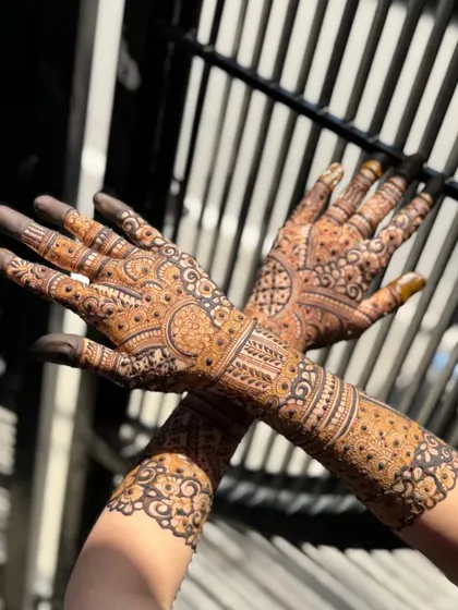 A shot of both hands crossed, showcasing the symmetry and detail of the bridal mehendi in natural sunlight.