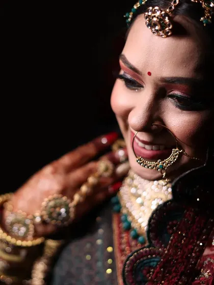 A close-up portrait of a smiling bride. The warm lighting highlights her intricate jewelry and the joyful expression on her face.