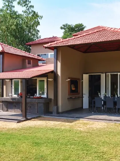 A side view of the Aishbagh home, revealing how the structure's silhouette and earthy tones harmonize with the landscape. The design uses covered verandas to create functional outdoor spaces for dining and relaxation.