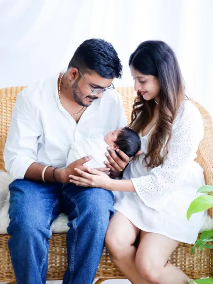 A bright and natural family portrait with a newborn. The parents are dressed in white and seated on a wicker couch, lovingly looking at their new baby, creating a fresh and modern family photo.