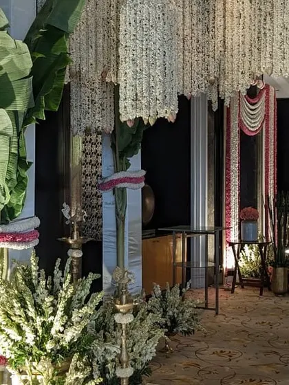 The entrance to a half-saree ceremony, adorned with fragrant jasmine garlands and banana leaves. The reflection on the polished floor doubles the beauty of this traditional South Indian decor.
