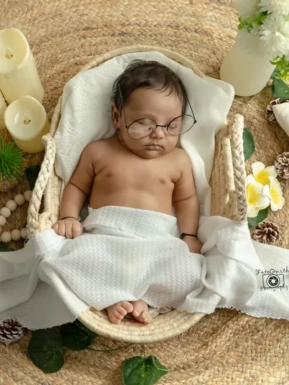A peaceful newborn in a simple, boho-inspired setup. The natural textures, soft white wrap, and gentle lighting create a serene and timeless portrait that focuses on the baby's delicate features.