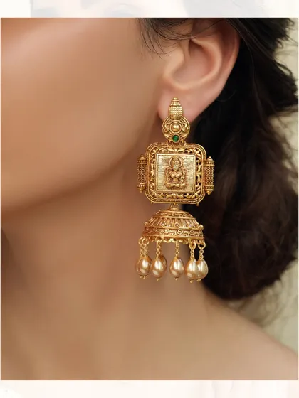 Classic temple-style jhumkas with a deity motif, crafted in gold-toned metal with pearl drops.