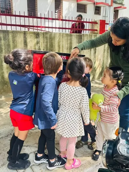 A teacher helps the children post their letters, explaining how the postbox works.