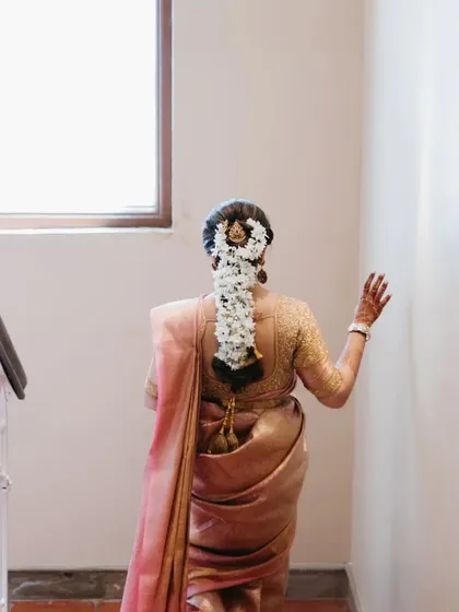 A back shot of a South Indian bride walking up the stairs, showcasing her traditional hairstyle adorned with a beautiful floral arrangement.