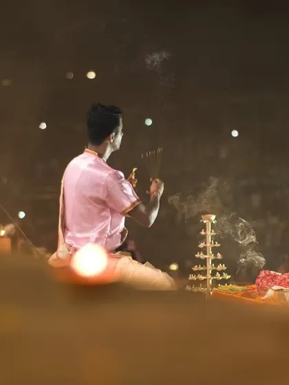 An over-the-shoulder view of a priest during the Aarti, with the crowd of devotees visible in the background. This perspective connects the ritual to the people.