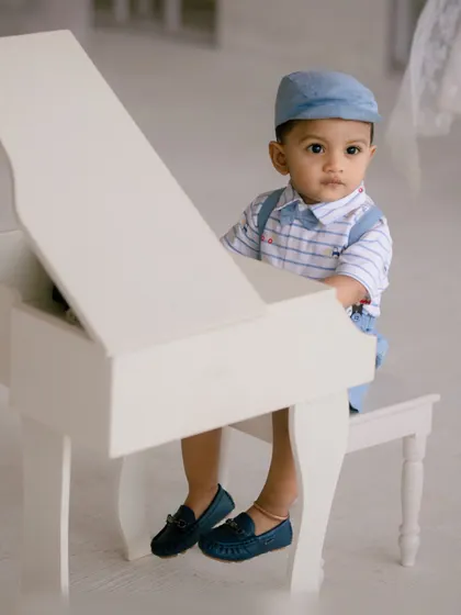A tiny pianist sits at his instrument, dressed smartly for his first birthday photoshoot.